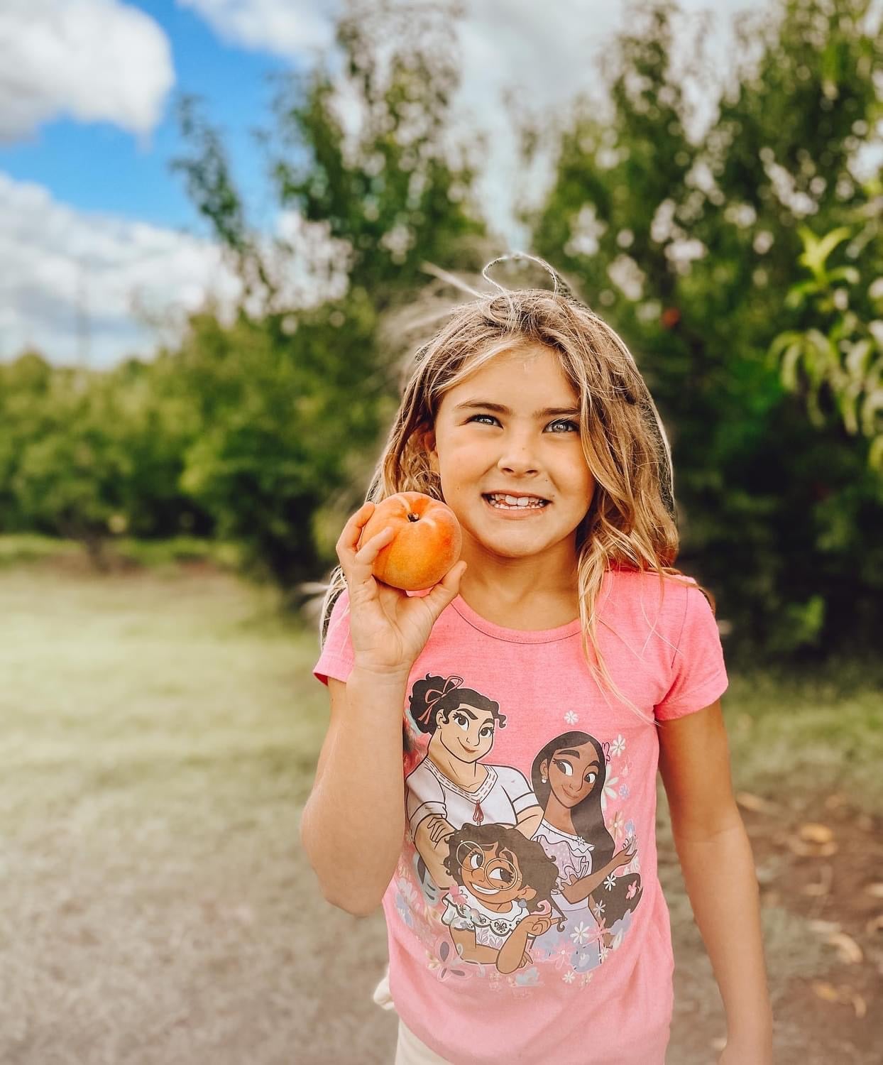 A girl in the orchard holding up an apple at Historic Weston Orchard