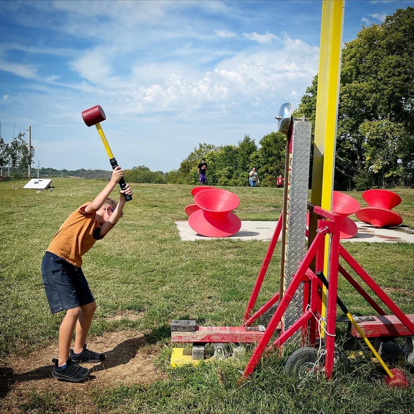 A kid swinging the mallet on the strength tester at Historic Weston Orchard