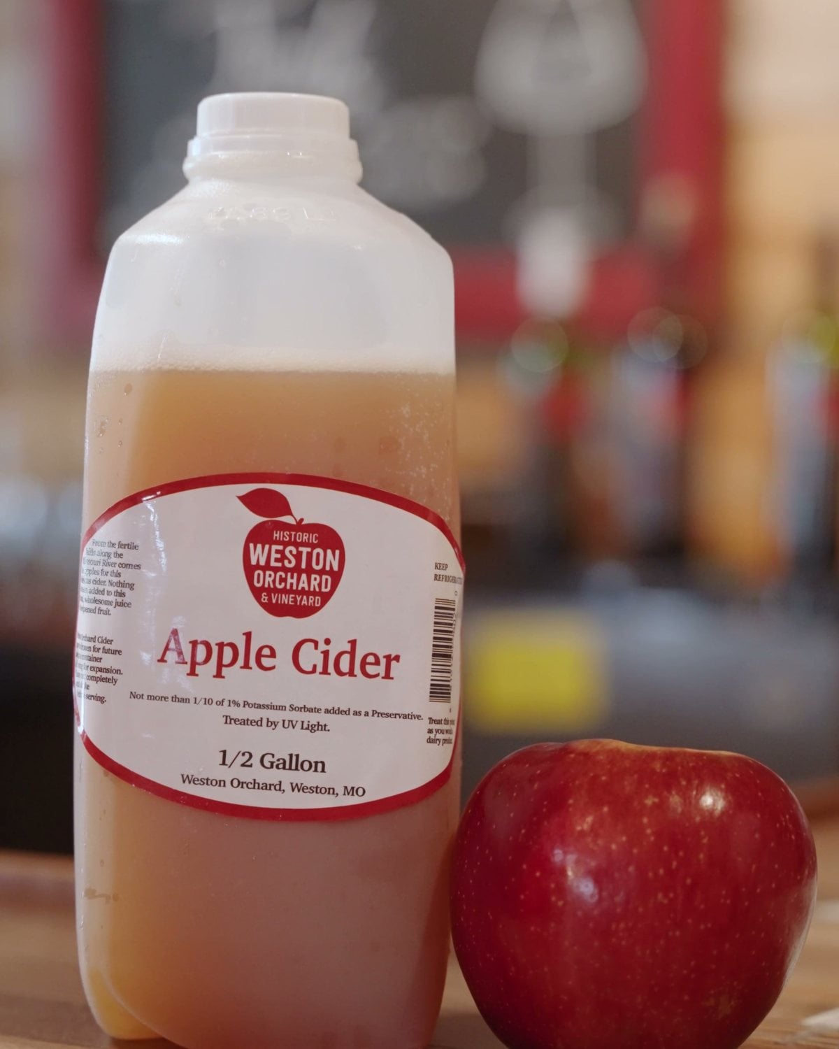 A half gallon jug of Historic Weston Orchard apple cider next to a red apple